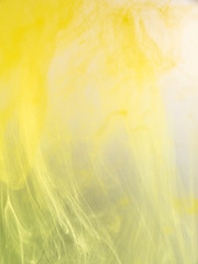 Abstract background of yellow paint dissolving into water, close up view. Blurred background. Acrylic abstract clouds moving in liquid. Yellow ink mixing with water. Abstract art