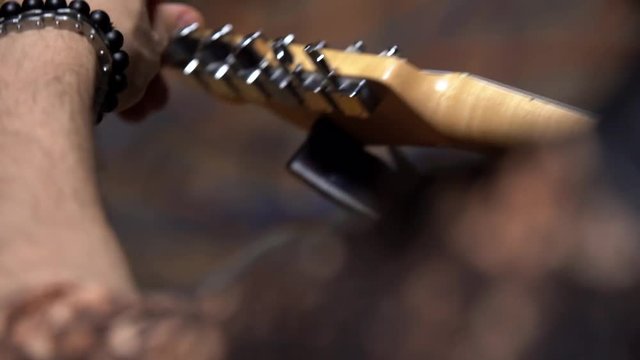 The musician puts on a guitar neck music tuner, twists the pegs and adjusts the guitar before the performance, close-up, shooting from the back