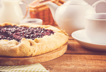 Homemade black currants tart. Vegetarian healthy galette. Delicious dessert with cup of tea and teapot on the wooden table.