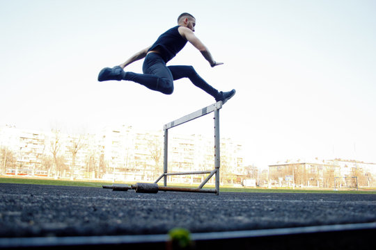 one caucasian male in a jump over a barrier. running on the stadium. Track and field runner in sport uniform in flight. energetic physical activities. outdoor exercise, healthy lifestyle. hurdling