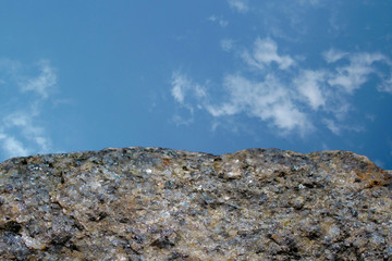 Rock or stone on blue sky with clouds background. Granite crouan rim or pick edge like cliff or...