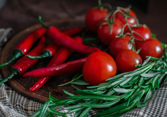 Fresh cherry tomatoes, sprigs of rosemary and chili peppers on a clay plate on the table. Fresh vegetables, herbs and spices - the concept of healthy eating. Food Photography