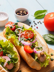 Close up view of homemade hotdogs with chicken sausages, fresh vegetables on blue wooden background. Hot-dogs with tomatoes, onion, basil, letucce and spices. Vertical.
