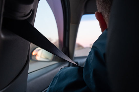 The Driver Is Wearing A Seat Belt. Back View. Sunset In The Car Mirror