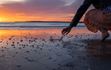 A woman cleaning a beach full of plastic bottles and rubbish in the sea