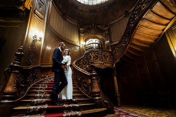 stylish luxury bride and handsome elegant groom on old wooden stairs on the background of luxury interior