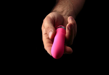 Pink vibrator in male hand on black background with artistic light
