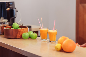 Two servings of fruit juice with a straw in glass cups stand on the bar near the fruit vases. Detox cleansing concept