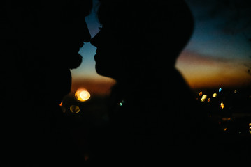 silhouette of happy couple looking at each other and touching with gentle on background of sunset sky and city lights