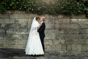 happy gorgeous blonde bride and stylish handsome groom with true emotions on background of old city wall