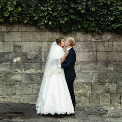 happy gorgeous blonde bride and stylish handsome groom with true emotions on background of old city wall