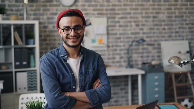 Portrait of happy business owner good-looking bearded guy standing in creative office with arms crossed smiling and looking at camera. People and workplace concept.