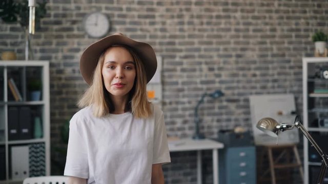 Portrait of cute girl hipster in modern hat standing in office room alone smiling and looking at camera. Millennials, workspace and beautiful people concept.