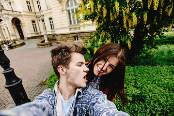 Fototapeta premium stylish happy hipster couple having fun traveling and taking selfies in the old city in europe in sunny spring time