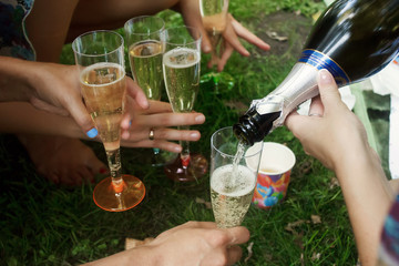 hands of woman holding colorful glasses and pouring champagne at joyful party in summer park, bridal shower or wedding reception