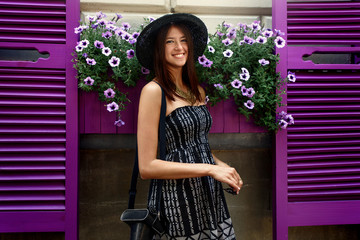 happy stylish woman hipster standing at colorful cafe with flowers in sunny street, summer travel concept