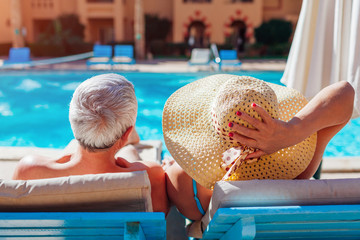 Senior couple relaxing by swimming pool lying on chaise-longues. People enjoying summer vacation. - Powered by Adobe