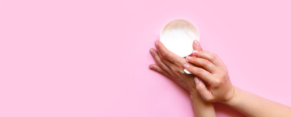 Woman's hands moisturizing cosmetic cream, lotion on a pink background with copy space, beauty, care concept. Pattern flat lay top view long banner