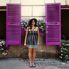 happy stylish woman hipster standing at colorful cafe with flowers in sunny street, summer travel concept