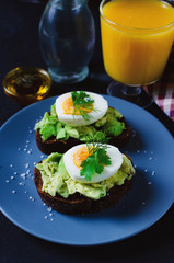 Healthy healthy snack (breakfast) - a sandwich with avocado and egg on a gray plate and a glass of fresh orange juice.