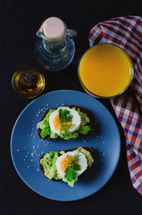 Healthy healthy snack (breakfast) - a sandwich with avocado and egg on a gray plate and a glass of fresh orange juice.
