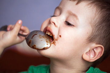 Close up portrait of Cute little boy eating chocolate yogurt at breakfast. Face messy with...