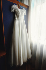 beautiful white luxury wedding dress on hanger on the background of a window