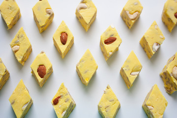 Yellow halva slices with almond and cashew nuts abstract rhombus pattern on white background