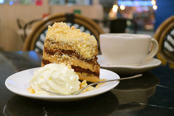 Plate of banoffee pie cake and whipped cream with blurry coffee cup in background