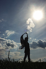 silhouette of stylish girl holding scarf in the windy evening outdoors in spring field, life success happiness concept