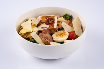 Selective focus Caesar salad with roasted chiken, bacon, quail eggs, lettuce leaves, chips, parmesan, cherry tomatoes on the white round plate close up