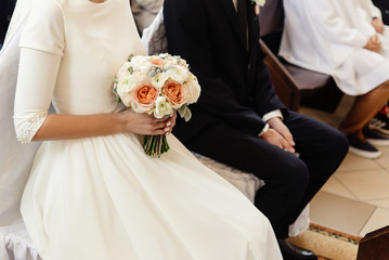 happy stylish bride and elegant groom sitting at catholic wedding ceremony at church