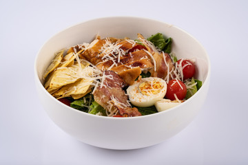 Selective focus Caesar salad with roasted chiken, bacon, quail eggs, lettuce leaves, chips, parmesan, cherry tomatoes on the white round plate close up