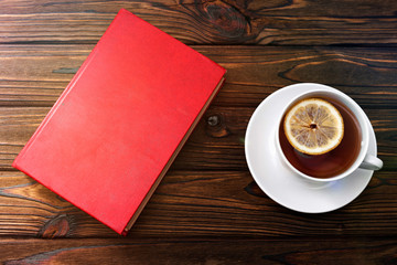 A book, a Cup of tea with lemon on the background of a wooden table.leisure, education, hobby. literature.