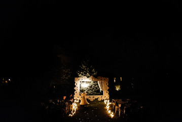 candle light in glass lanterns and wooden arch and lamp at luxury wedding ceremony in evening, decor and arrangements