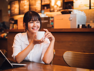 Asian woman drinking coffee in cafe and using laptop computer for working business online marketing
