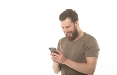 Typing text message. Smiling man with beard standing on white background and holding mobile phone.