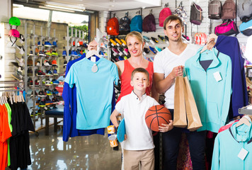 man and woman with boy choosing t-shirts and other goods in sport shop