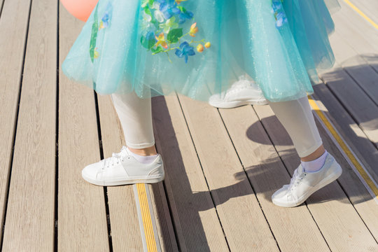 Woman in white sneakers and blue fatin skirt steps up the stairs. Spring street fashion