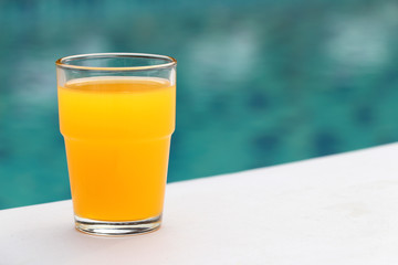 The glass of orange juice is placed on the seat of the chair located by the pool.