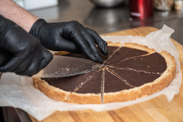Cheef's hands in black latex gloves cutting chocolate cake