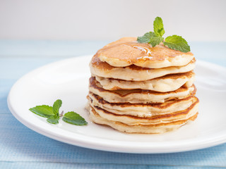 Pancakes stacked and topping with honey,mint leaf  on the white plate and blue wooden table. Homemade pancake.