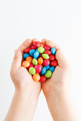 Multicolored candies in the hands of a child on a white isolated background