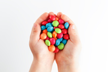 Multicolored candies in the hands of a child on a white isolated background