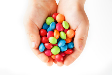 Multicolored candies in the hands of a child on a white isolated background