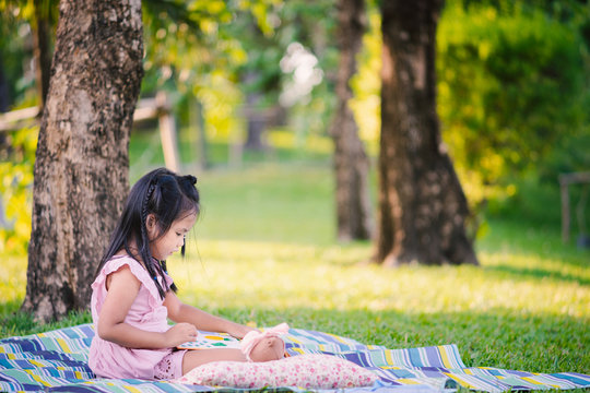 A little cute girl reading a book sitting under the tree