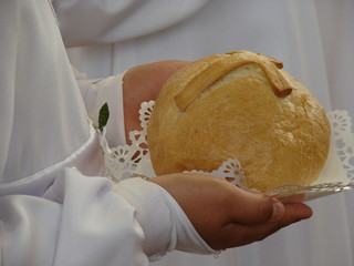 Chleb ze znakiem krzyża w rękach dziecka w białej szacie podczas uroczystości Pierwszej Komunii  Swiętej - obrazy, fototapety, plakaty
