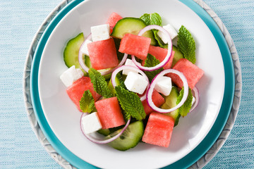 watermelon salad with feta cheese,mint,onion and cucumber on blue background. Top view. Close up