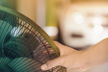 Hand of Young man touch and adjust  on front grills of electric fan for a good wind in his home in summer of april in Thailand.
