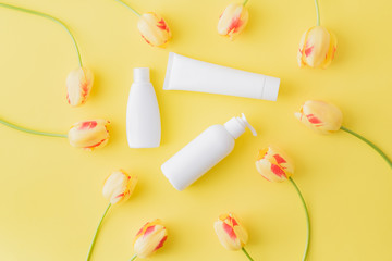 Flat lay composition with cosmetic products, mockup white tubes and yellow tulips on a yellow background